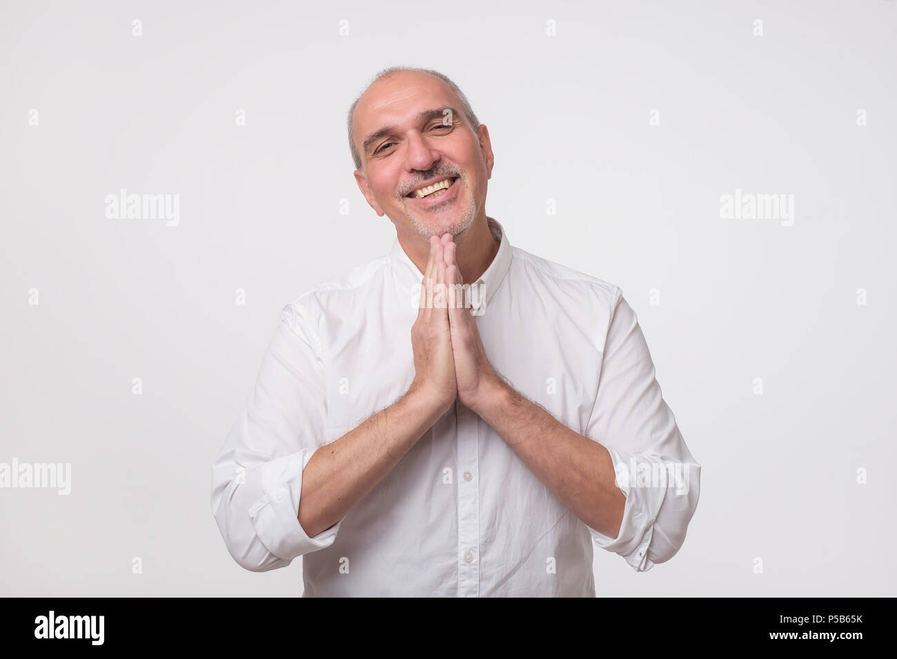 Closeup portrait of desperate mature man in white shirt showing clasped hands,asking for help or excuse. Stock Photo