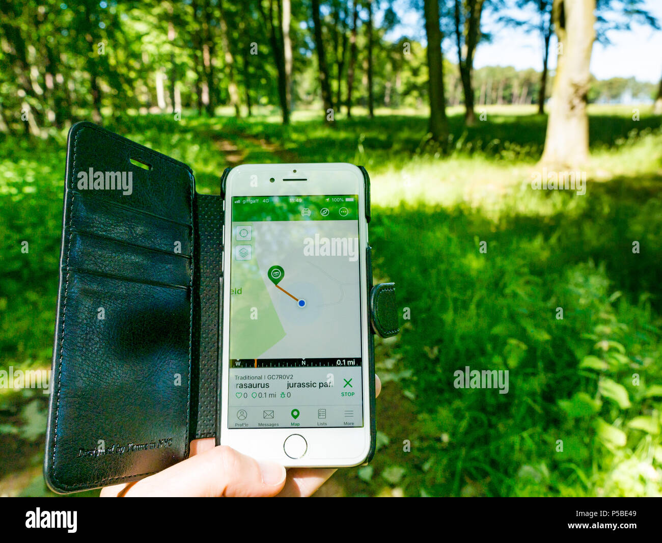 Close up of woman's hand holding a mobile phone using geocaching app map showing a cache nearby with blurry countryside path, Scotland, UK Stock Photo