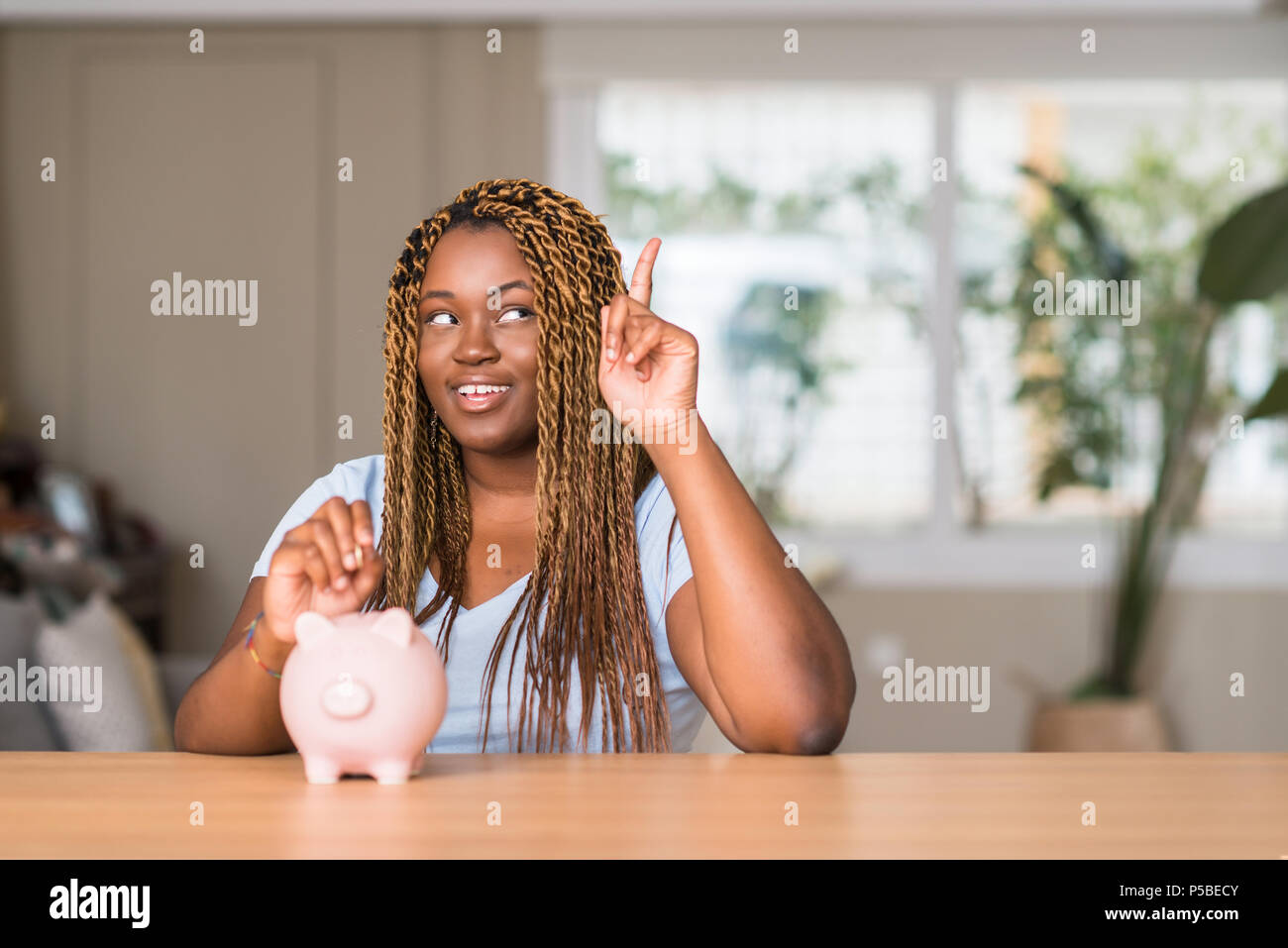 African american woman saving money with piggy bank surprised with an ...