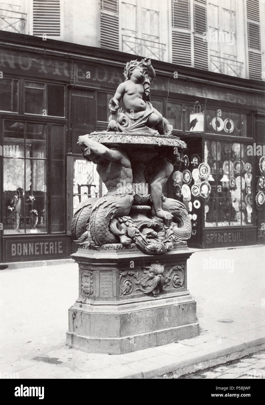 Fontaine No. 1 Rue du Fbg. [i.e. Faubourg] St Martin (fonte). No. 16. English: Cast iron fountain on curb of city street, plinth supportingmale figures with fish tails supporting bowl holding a child figure with shells. Inscription on plinth. Shop front in background. circa 1865. N/A 327 Charles Marville, Fontaine No. 1 Rue du Faubourg-Saint-Martin, ca. 1865 Stock Photo