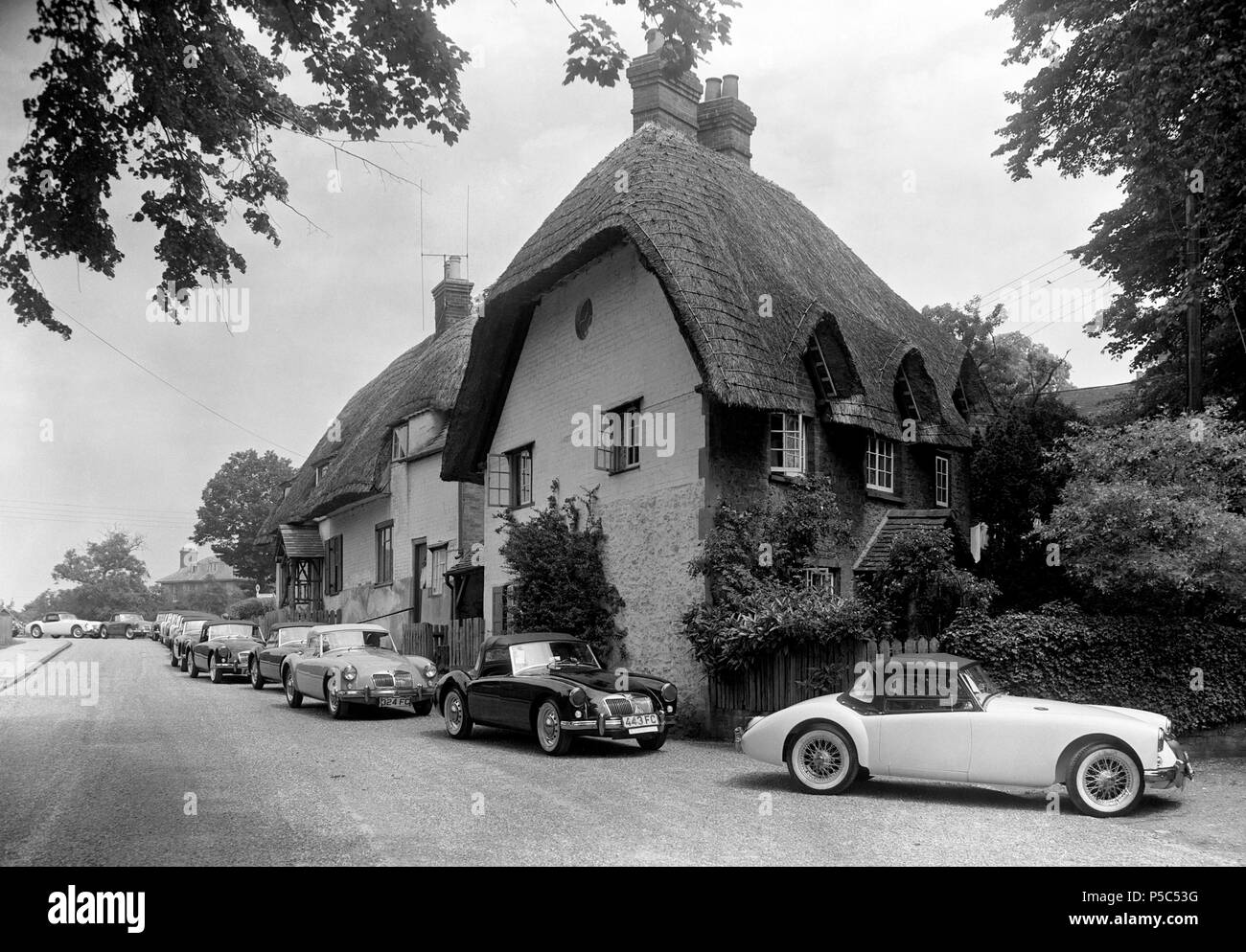 The old-world thatched roofs in the Oxfordshire village of Clifton Hampden contrast with the sleek modern lines of the MG sports cars passing through from the factory at Abingdon on their way to the docks, ready to be exported to the North American markets. Stock Photo
