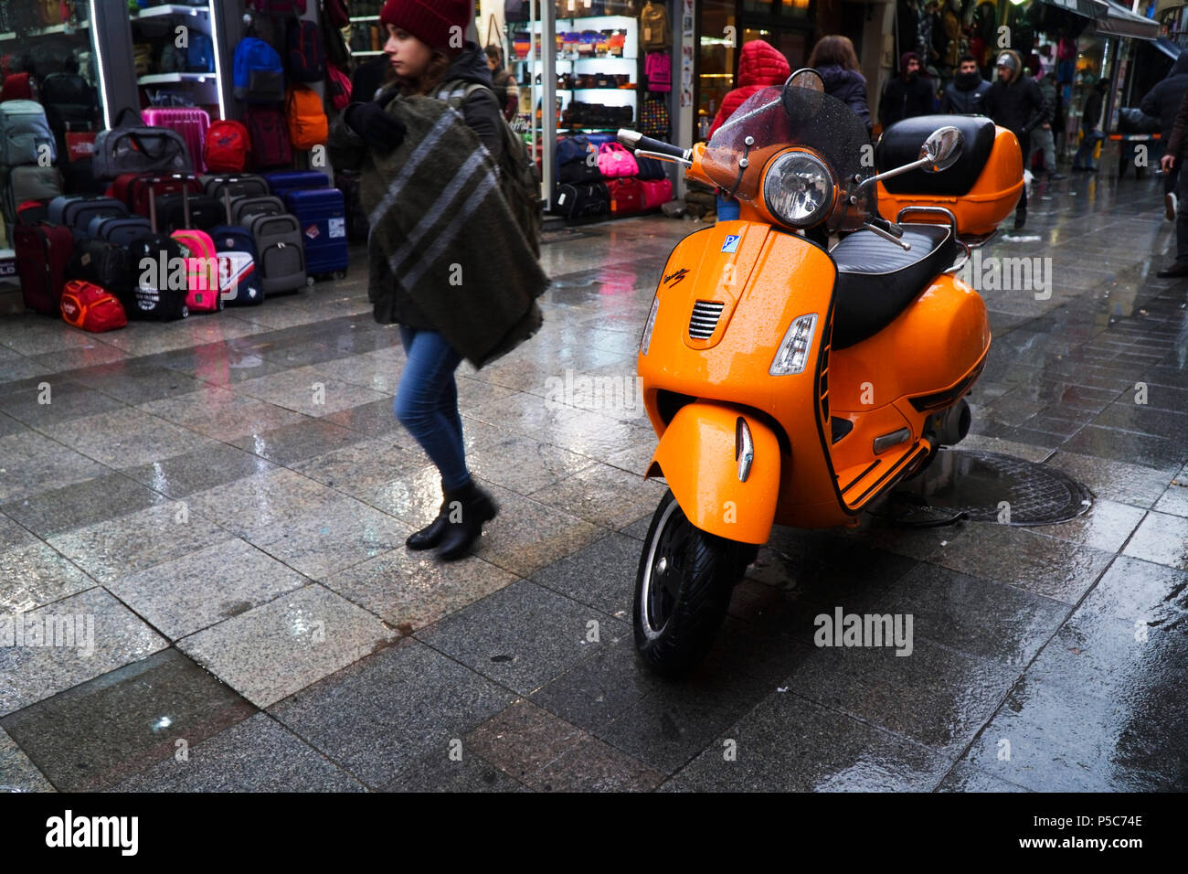 Istanbul, Turkey - December 31, 2016: Details of a wet orange Piaggio Vespa S in a rainy day at Istanbul Kadikoy. A young girl is passing. Stock Photo