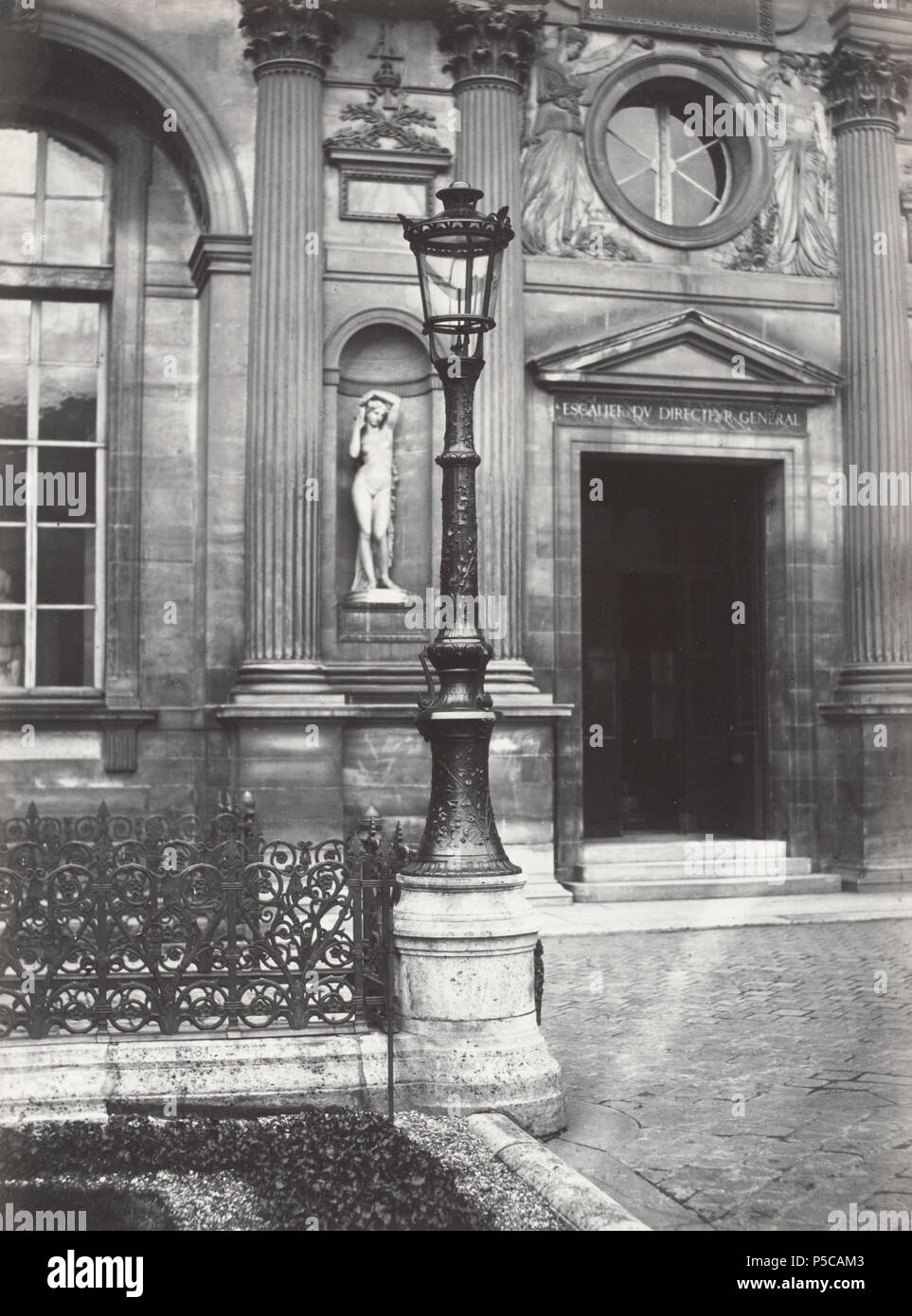 Louvre, (ancienne cour. escalier du Dr. [i.e. Diréctéur General]) no. 64. English: Single lantern on decorative iron lamp post mounted on stone base, wrought iron grille on left, doorway in right background with classical style statue in niche beside door. Niche statue: Bathsheba (1859), by Eugène Oudiné (1810-1887). North façade of the Cour Carrée in the Louvre palace, Paris. 1878. N/A 327 Charles Marville, Louvre, ancienne cour, 1878 Stock Photo