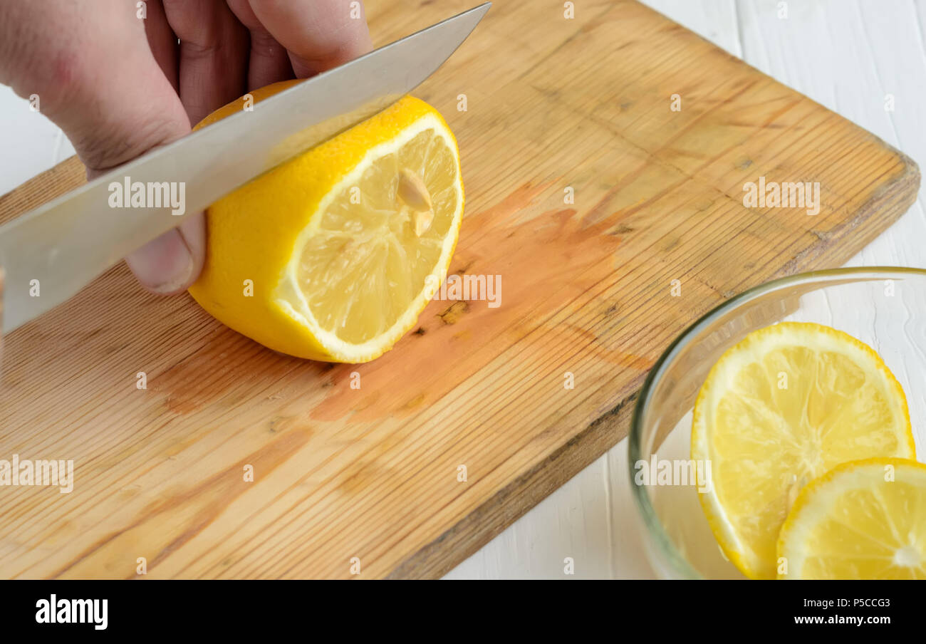 Someone cutting a lemon on the chopping board.Two slices of lemon into glass plate are down right angle. Stock Photo