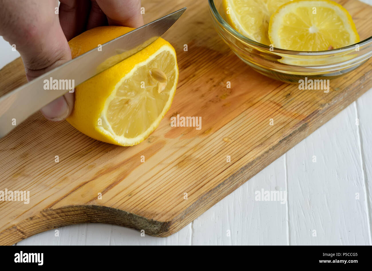 Someone cutting a lemon on the chopping board.Two slices of lemon into glass plate are top right angle. Stock Photo