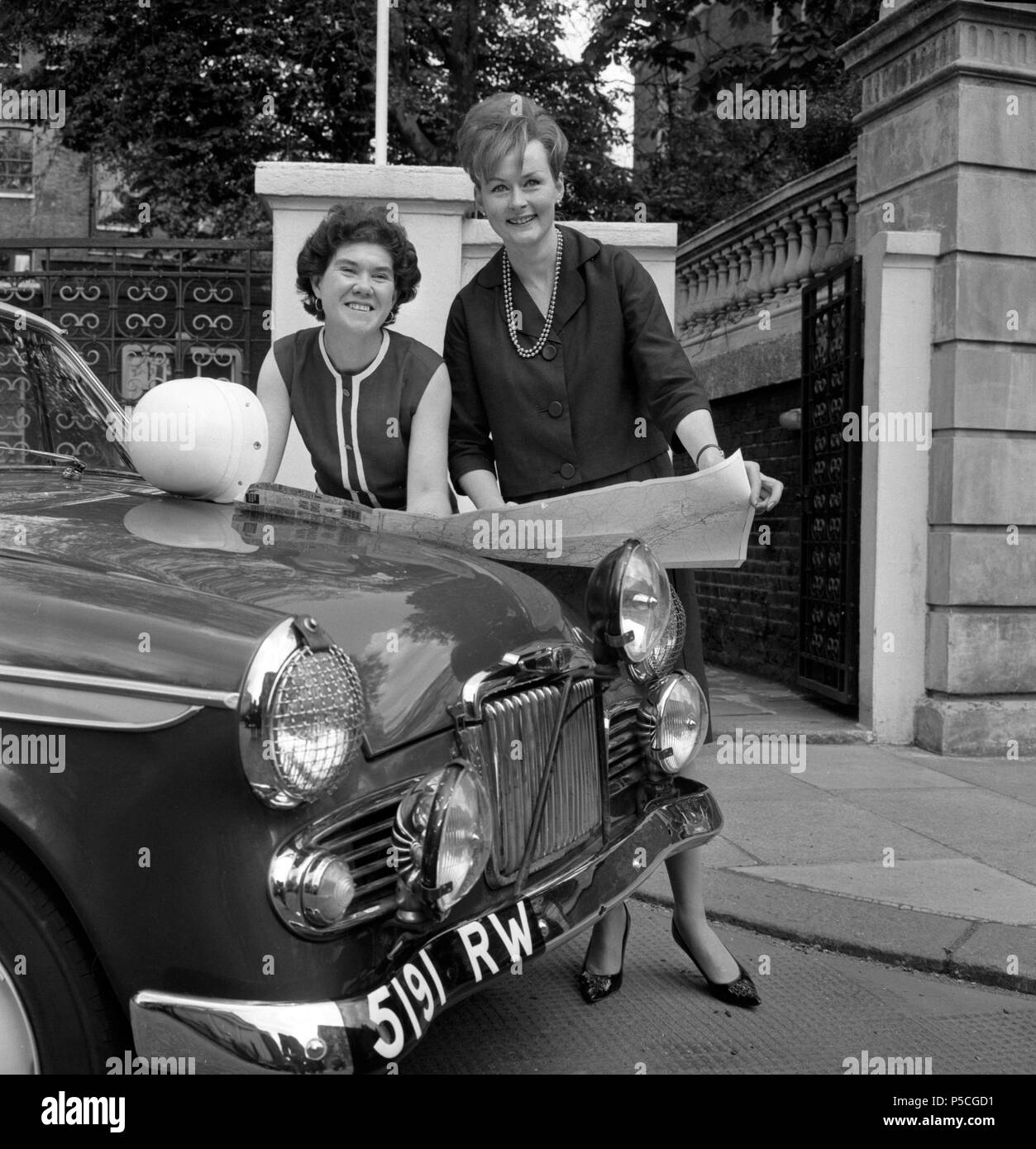 Dublin-born Rosemary Smith (r), 24, and Rosemary Sears, 30, use the bonnet of their Sunbeam Rapier to study maps of the route they will take as the Rootes Group women's team in the International Greek Acropolis Rally. Stock Photo
