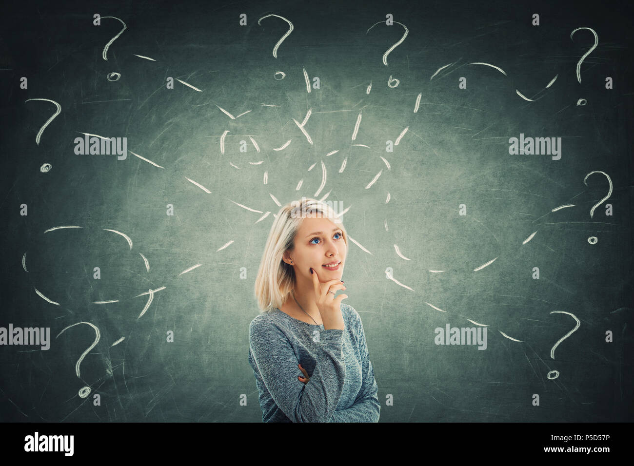 Puzzled young woman in front of a blackboard try to solve different tasks, having a lot of questions. Inspiration concept and self development. Stock Photo
