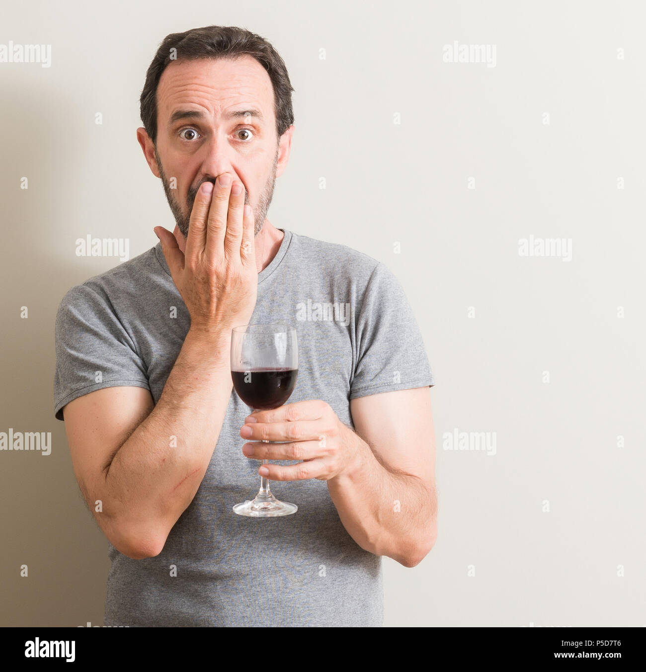 Senior man drinking red wine in a glass cover mouth with hand shocked
