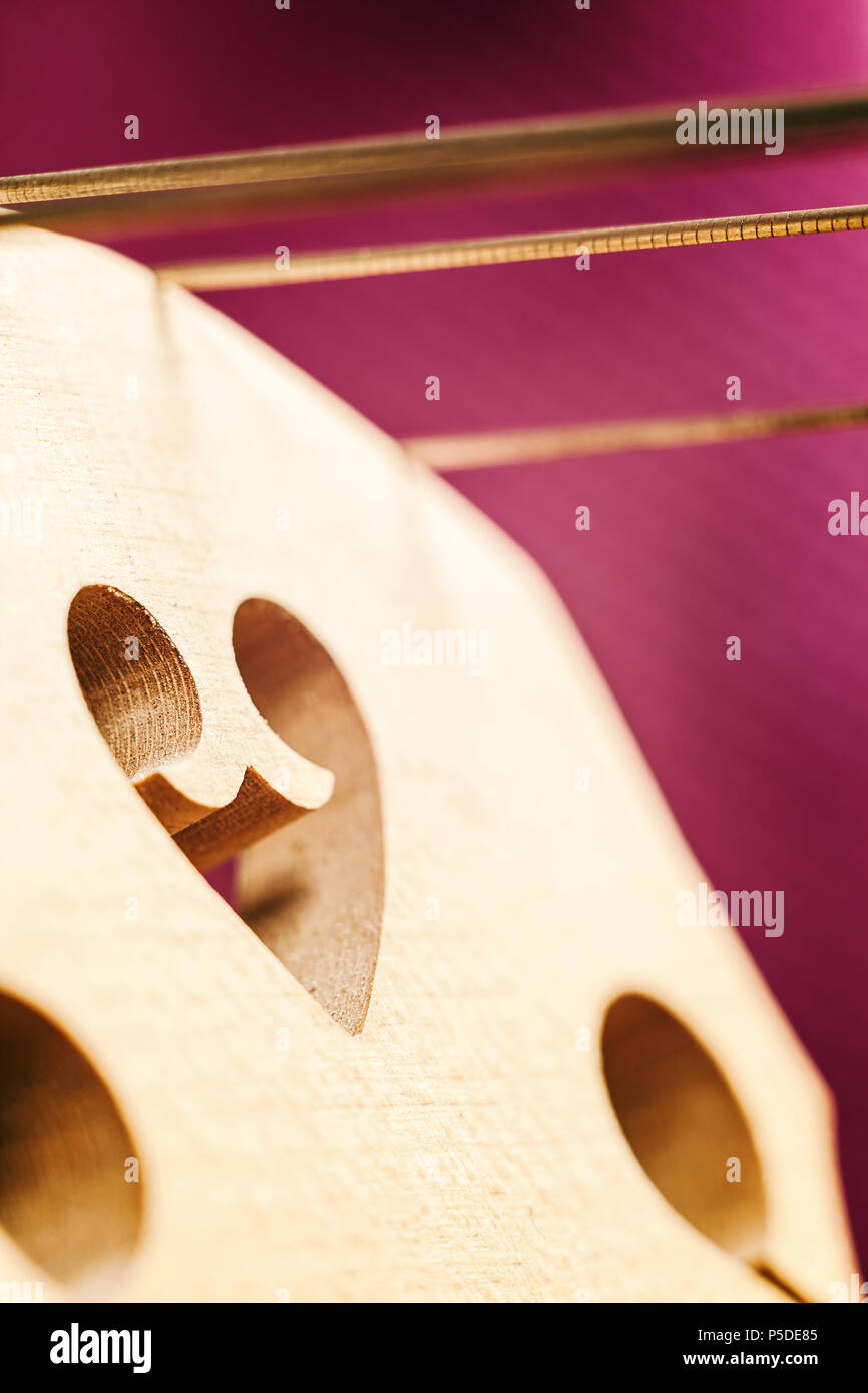 Details of a cello bridge with strings on purple background Stock Photo