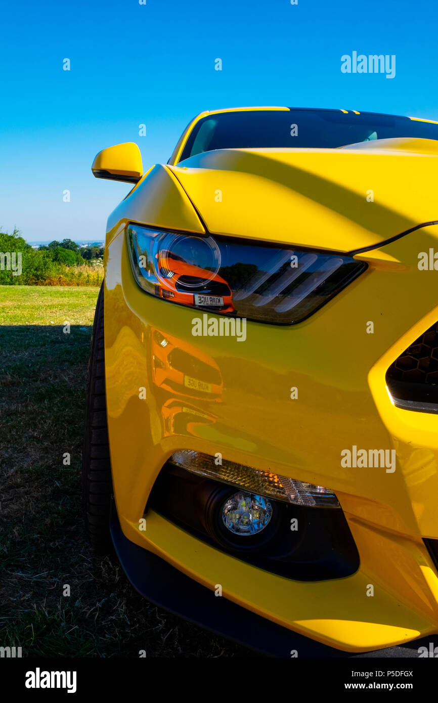 A yellow Ford Mustang 5 litre V8 GT Fastback Auto with a 2nd orange Ford Mustang reflected in the headlight lens Stock Photo