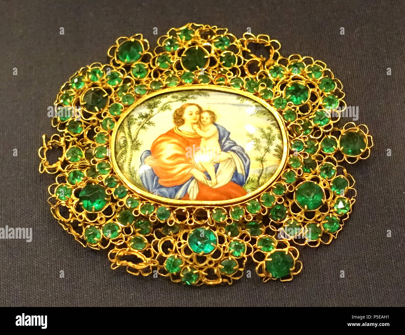 N/A. English: Exhibit in the Museo Nacional de Artes Decorativas, Madrid, Spain. This work is in the  because the artist died more than 100 years ago. Photography was permitted in the museum without restriction. 10 October 2014, 06:08:39. Daderot 241 Brooch with Virgin and Child, 18th century AD, gold filigree, emeralds, enameled plaque - Museo Nacional de Artes Decorativas - Madrid, Spain - DSC08024 Stock Photo