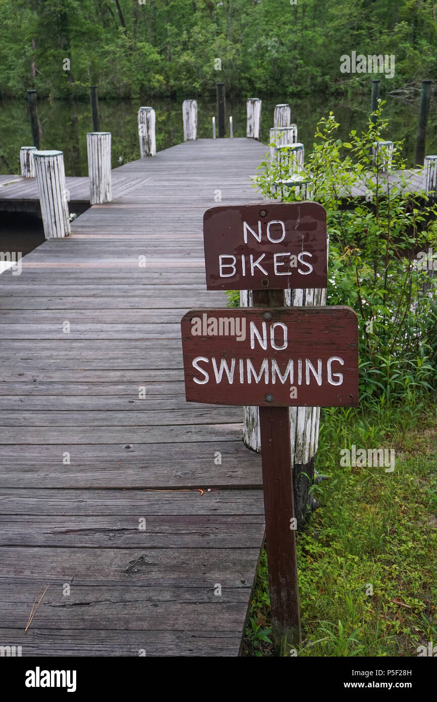 Pokomoke, Maryland, USA: Signs at a dock in the Pokomoke River State Park warn visitors that biking and swimming are not allowed. Stock Photo