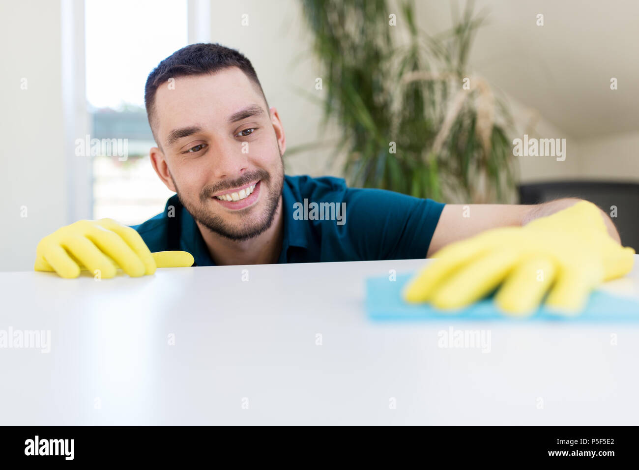 smiling man cleaning table with cloth at home Stock Photo