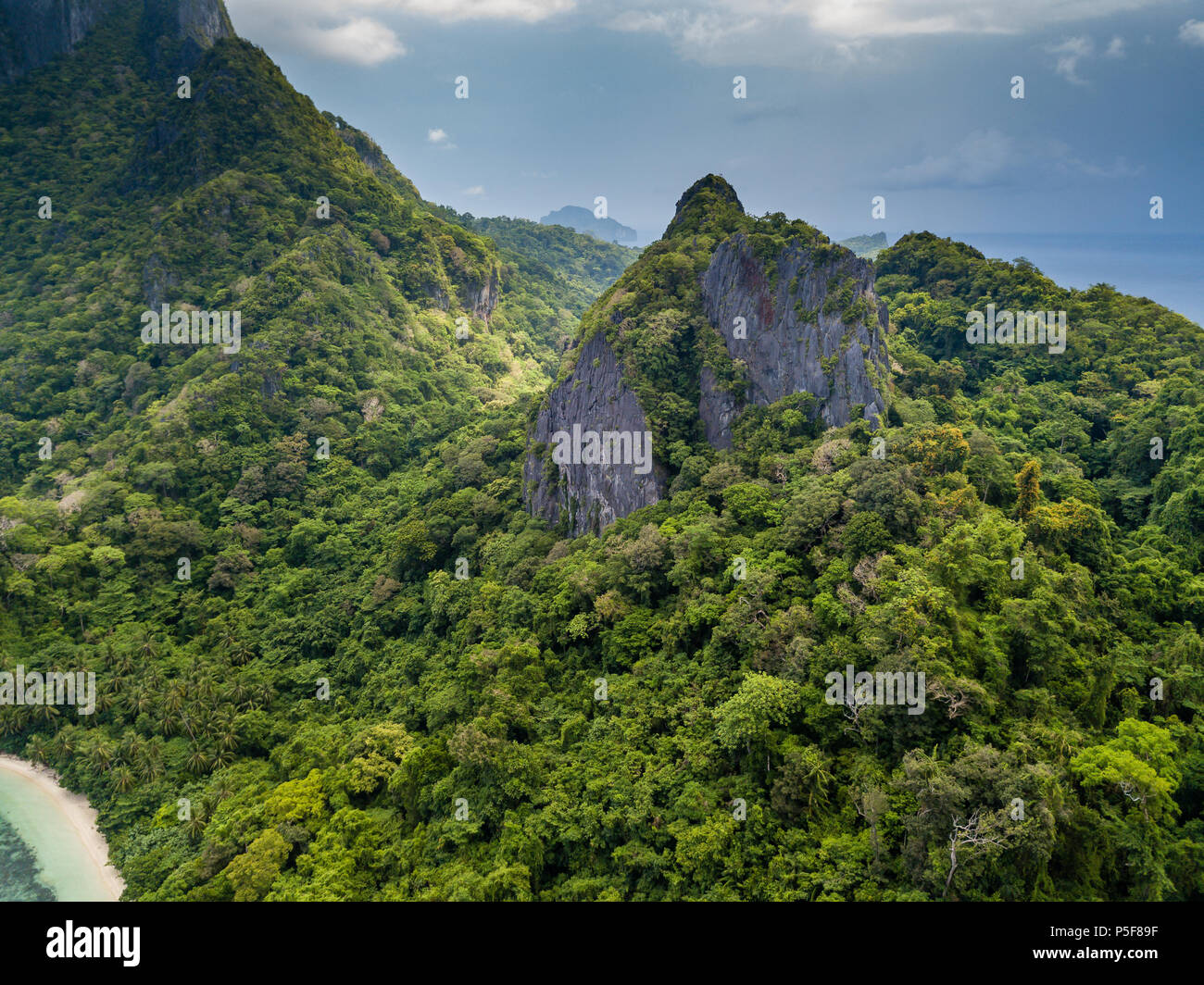 Aerial drone view of a remote tropical island with towering jagged limestone cliffs and jungle with a stormy sky Stock Photo