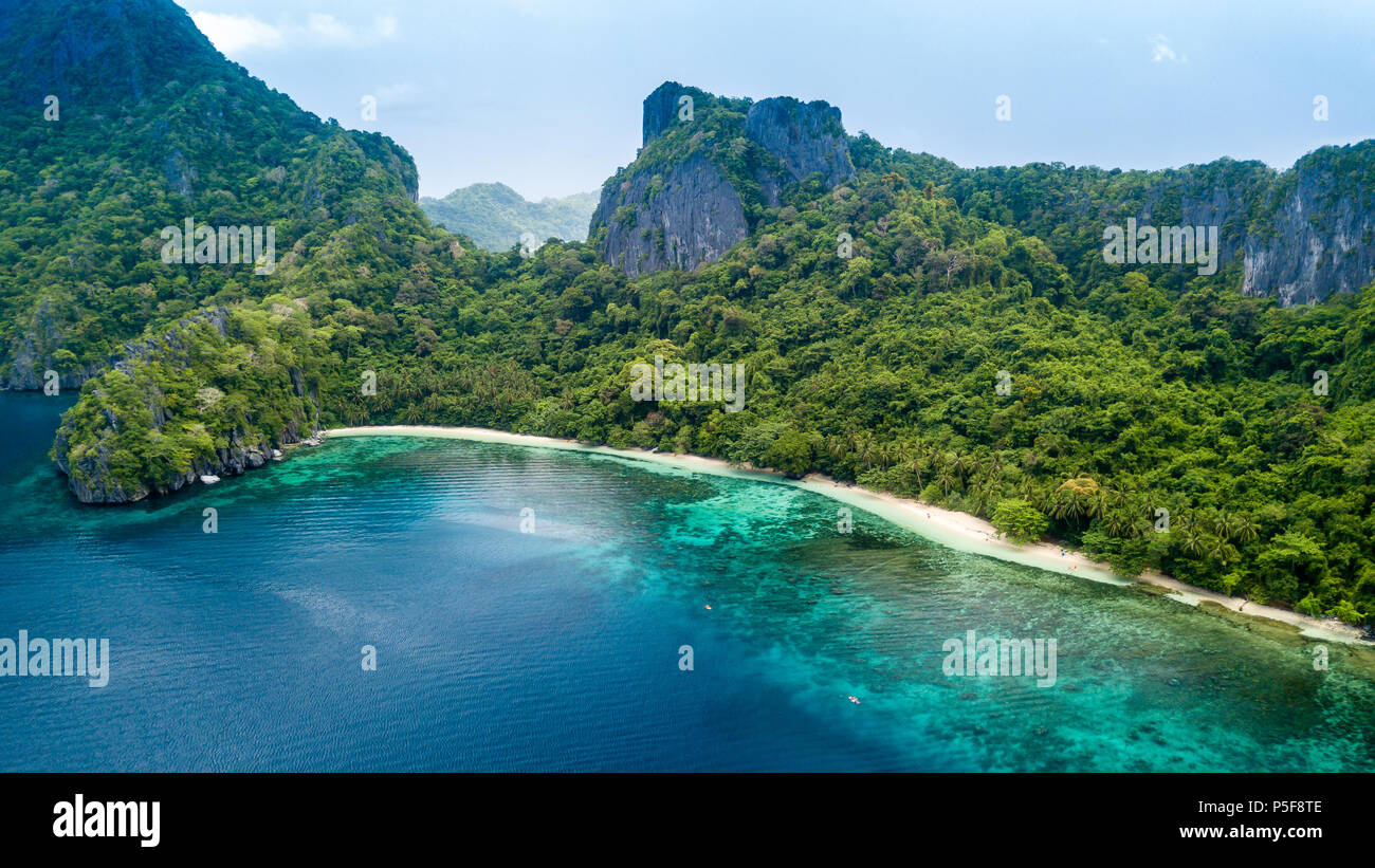 Drone view of a beautiful deserted tropical island with jungle, cliffs and fringed by coral reef Stock Photo