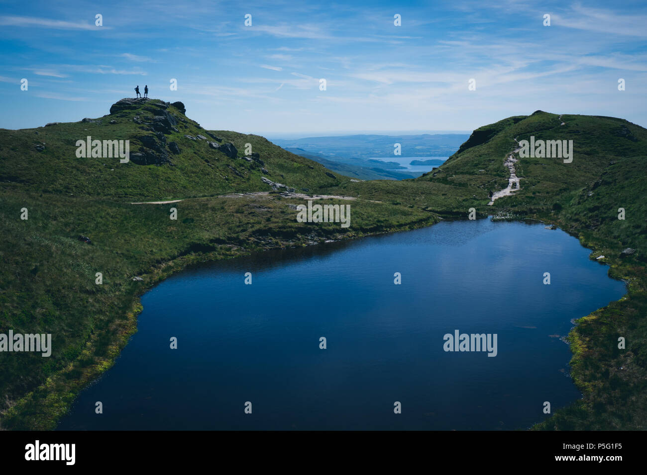Two hillwalkers stand on Ben Lomond, near the summit, at a lochan on the Ptarmigan route. Stock Photo