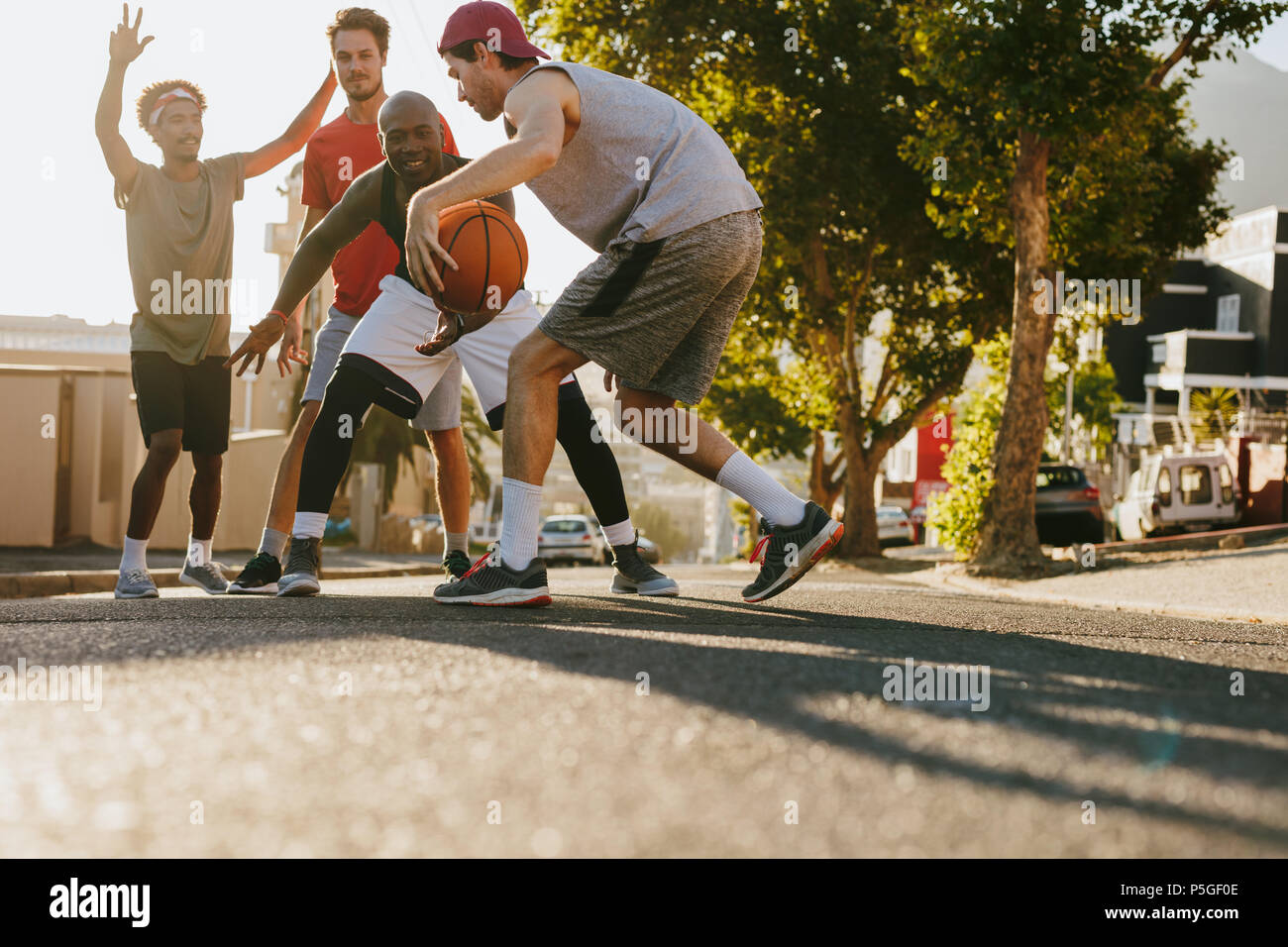 Men playing basketball game on a sunny day on an empty street. Men practicing basketball dribbling skills on street. Stock Photo