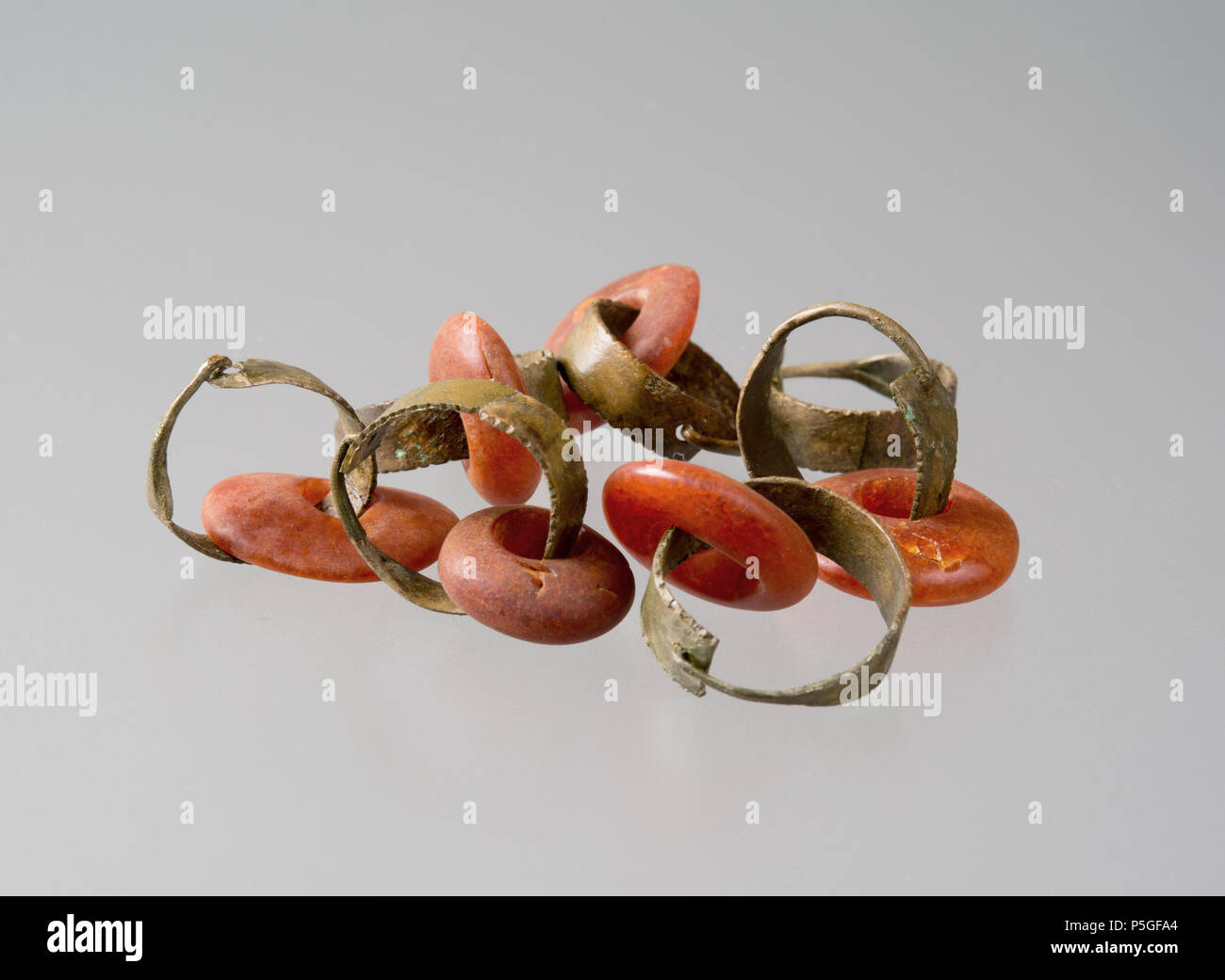 N/A. Nederlands: Zes barnstenen kralen met zeven koperen ringetjes, deel  van de inventaris van het graf van een vrouw uit Meteren, uit de IJzertijd.  De kralen en ringen zijn rond de schedel