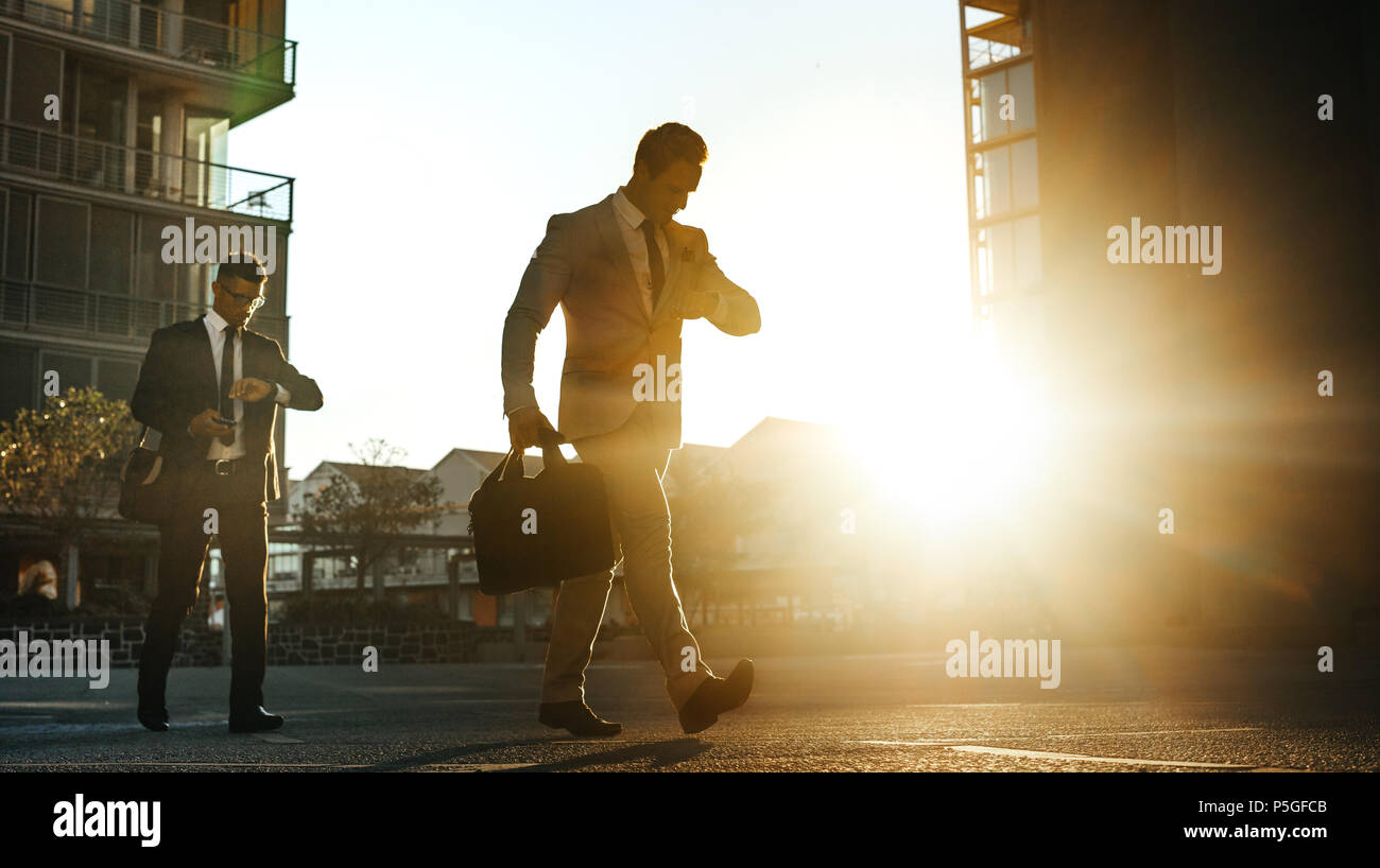 Men in formal clothes commuting to office early in the morning carrying  office bags. Businessman using mobile phone while walking on city street to  of Stock Photo - Alamy