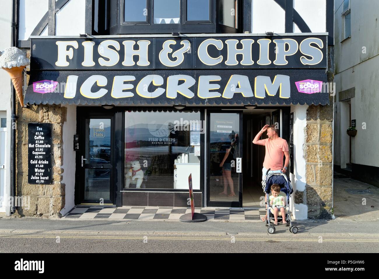 Father with young son in pushchair who is an eating ice cream outside an ice cream and fish and chip shop in Marazion Cornwall England  UK Stock Photo