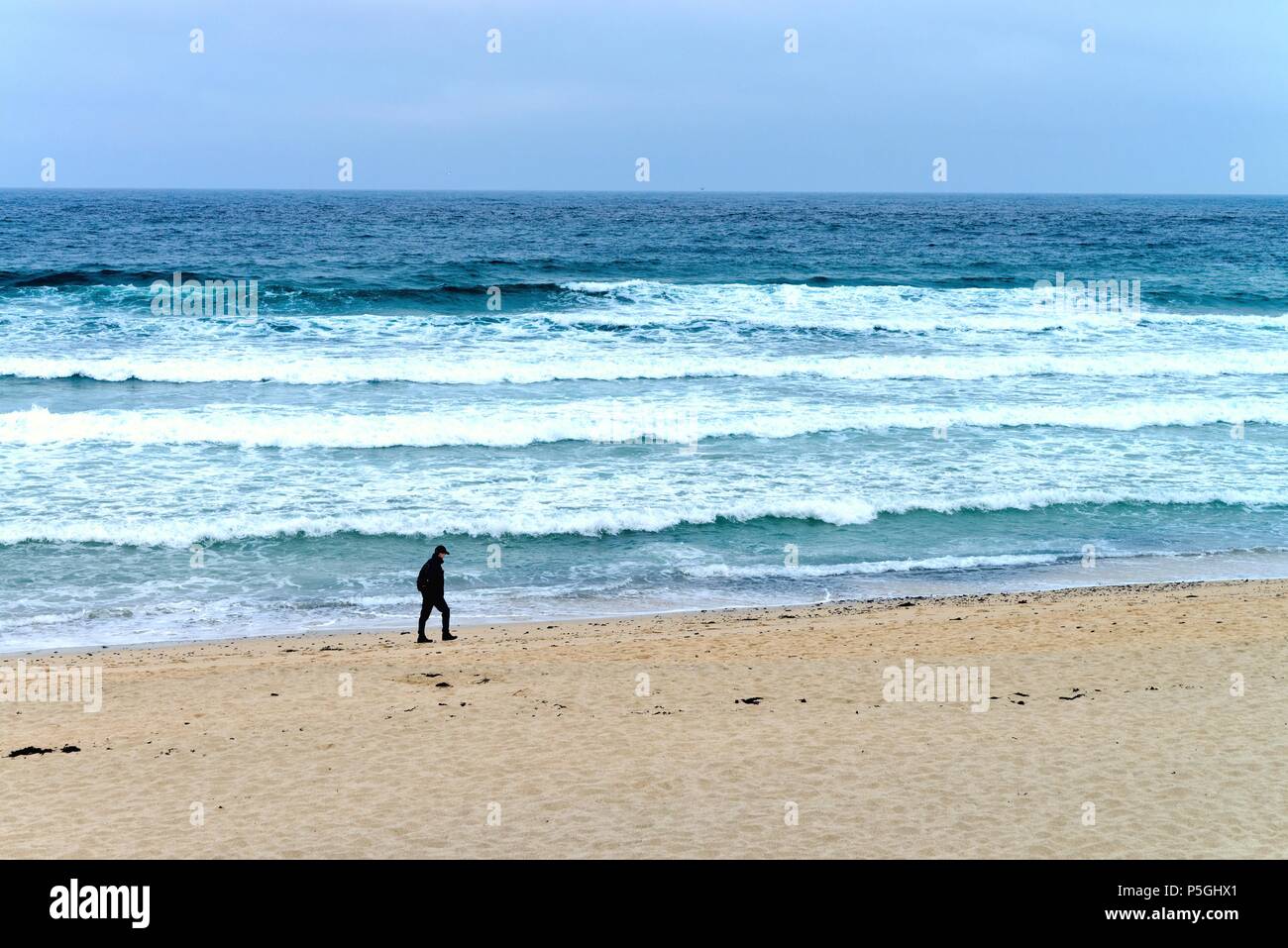 Solitary man walking along a sandy beach with breaking waves in the background St.Ives Cornwall England UK Stock Photo