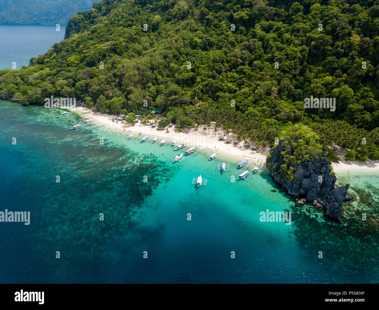 Aerial drone view of traditional Banca boats and coral reef surrounding a scenic tropical sandy beach (7 Commando Beach, El Nido) Stock Photo