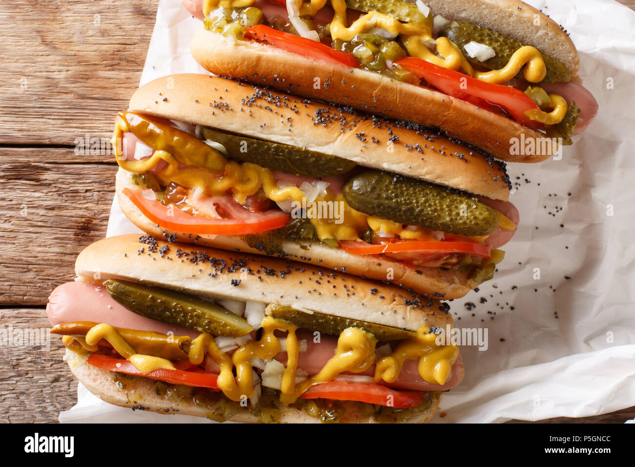 Homemade Chicago style hot dogs with mustard, tomatoes, pickled cucumbers, onions and relish close-up on the table. Horizontal top view from above Stock Photo