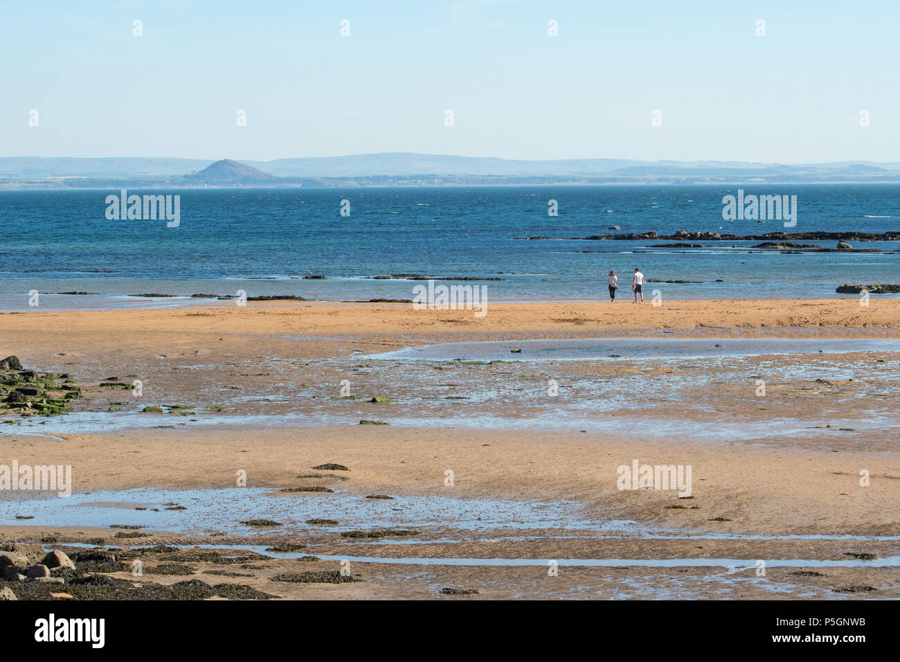 Firth of Forth - couple on Anstruther beach, Fife, looking across the Firth of Forth to North Berwick and the distinctive outline of North Berwick Law Stock Photo