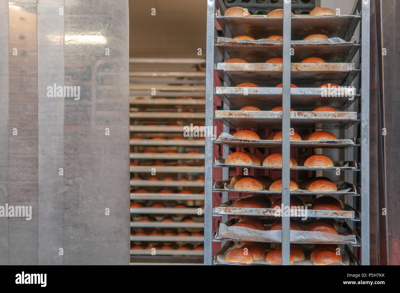 Freshly baked bread rolls on a baker's shelf trolley at a bakery. Stock Photo