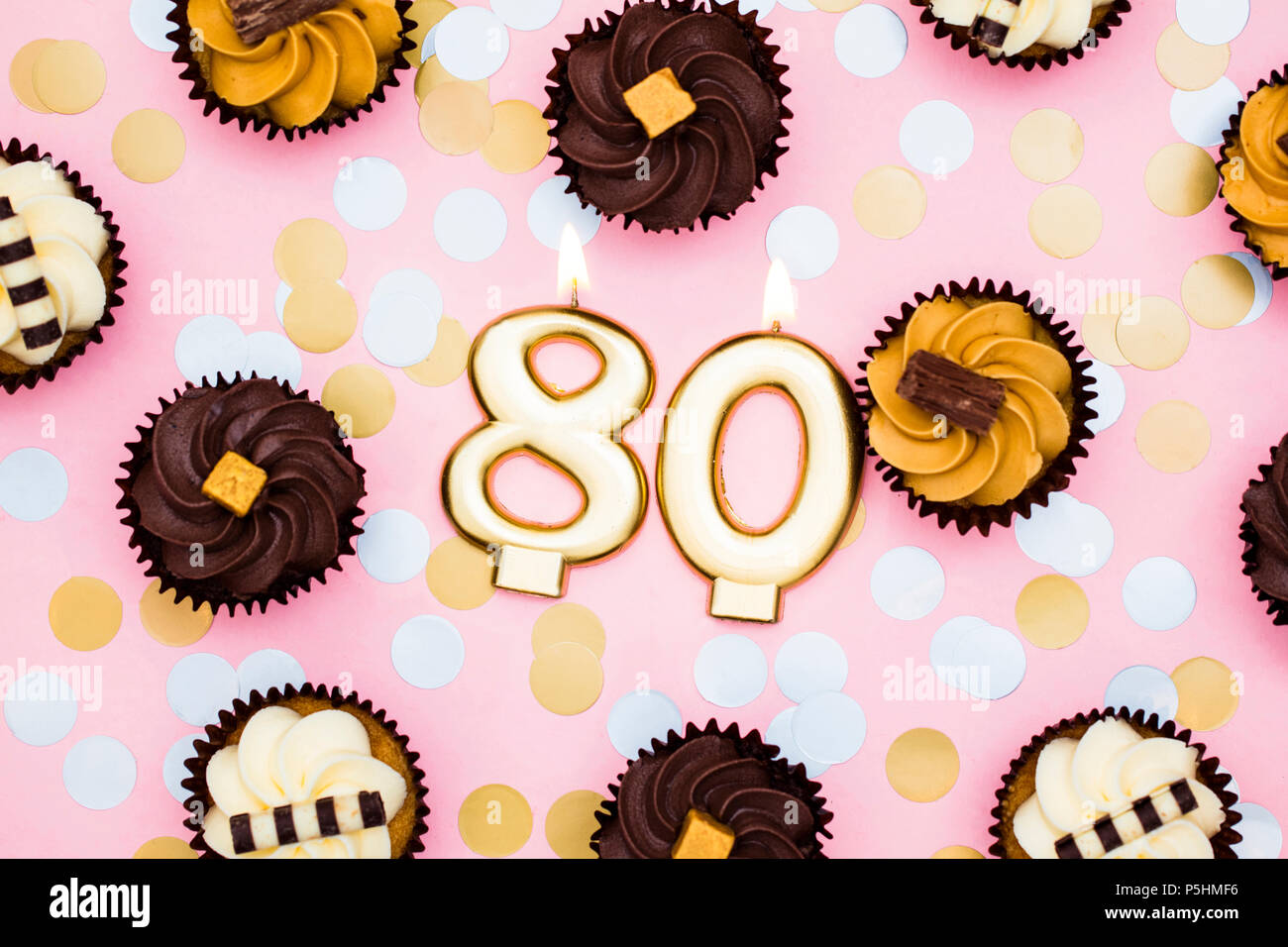 Number 80 gold candle with cupcakes against a pastel pink background Stock Photo
