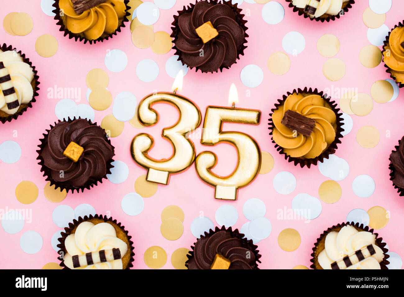 Number 35 gold candle with cupcakes against a pastel pink background Stock Photo