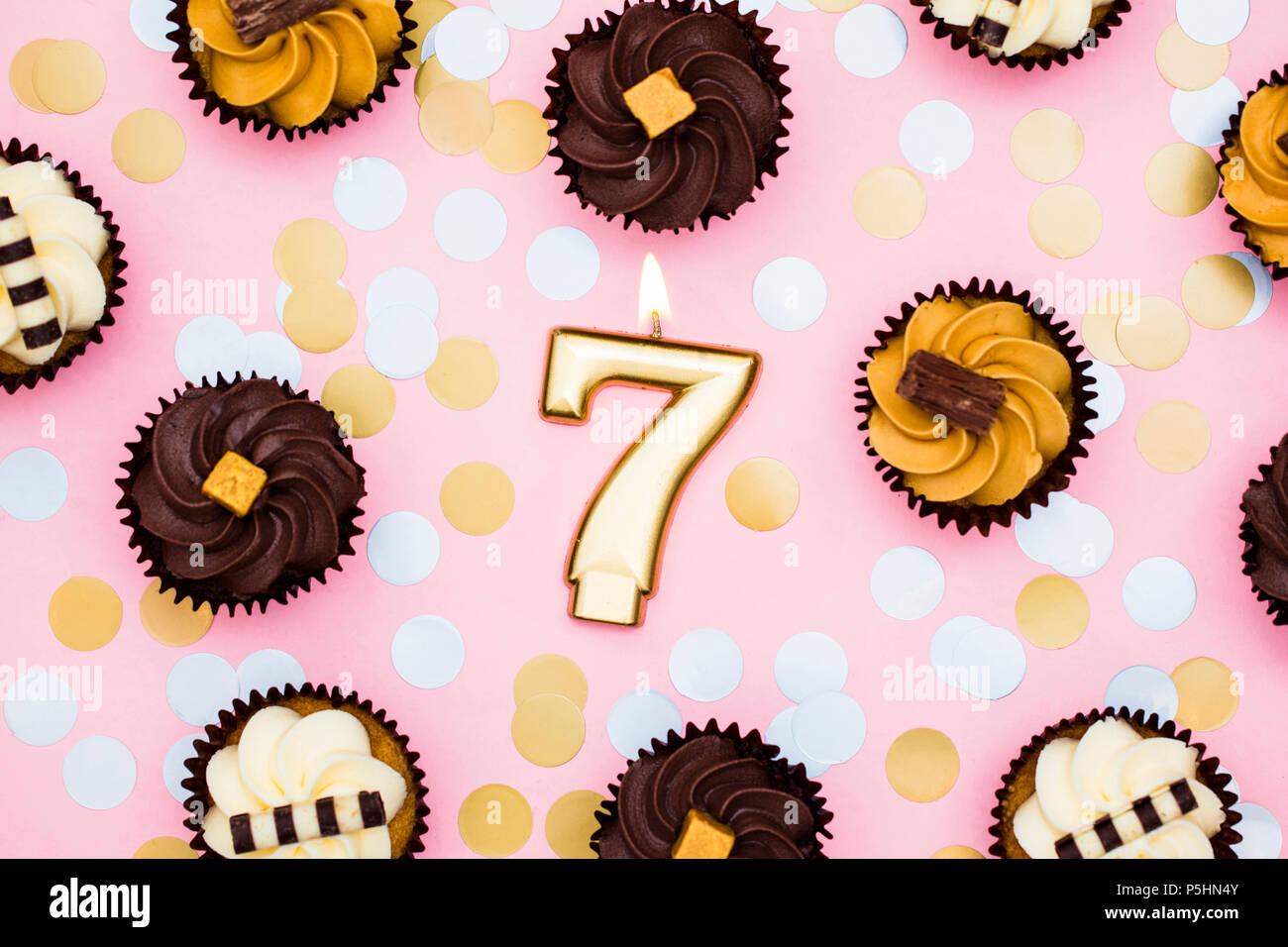 Number 7 gold candle with cupcakes against a pastel pink background Stock Photo