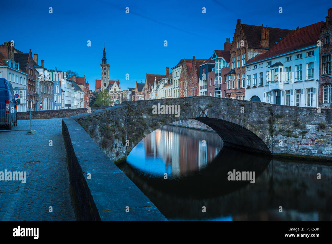 Beautiful panoramic view of famous Spiegelrei canal with famous Poortersloge and Jan van Eyck square in the background illuminated during blue hour at Stock Photo