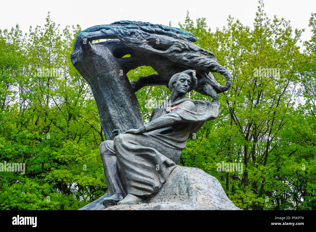 The Frederic Chopin monument by sculptor Waclaw Szymanowski, Royal Lazienki Park. Bronze statue surrounded by green trees and grey skies Stock Photo