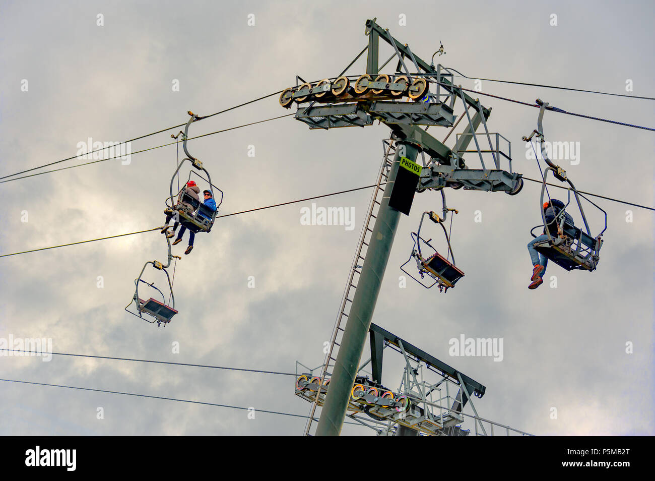Queenstown, NZ – April 15, 2018: Fun riders with their carts on a cable chair lift going up the hill top for a luge ride with mountains and snow. Stock Photo