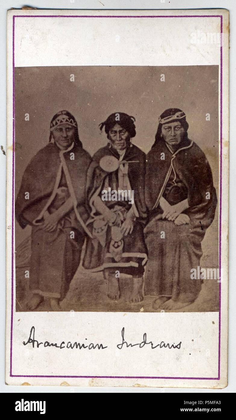 N/A. English: Photograph (black and white); carte de visite, three Mapuche women sitting in a studio; the women on the left wearing trarilonko (hair lace/headgear), quipan ( a square cloth, wrapped around the body), trarihue (waistband) and ikulla (shawl); elderly woman in centre wearing trarilonko or lloven nitrowe (women´s headdress), chaway (earrings), tupu (clothes pin), pentreor (chest hanging of three chains), quipan, trarihue, and ikulla; she is holding two bags; woman on right wearing trarilonko, quipan, trarihue, and ikulla; Pampas, Argentina or Chile. Unknown date. Christian Enrique  Stock Photo