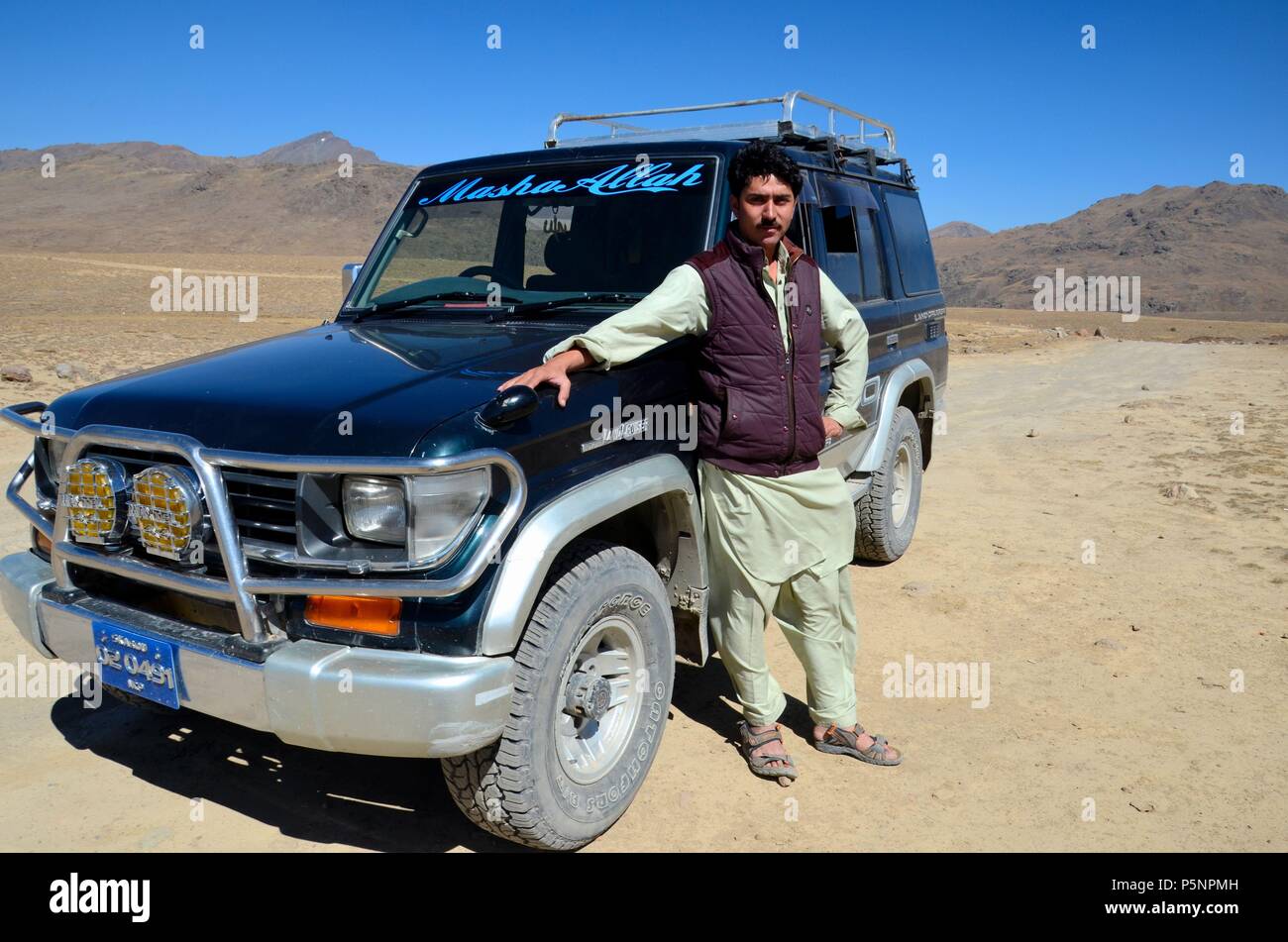 Pakistani tourist jeep driver in salwar kameez poses with jeep at Deosai Plains national park desert Skardu Pakistan Stock Photo