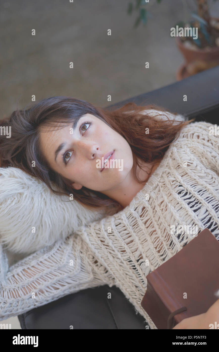 Tired young woman lying on a sofa with a book Stock Photo - Alamy