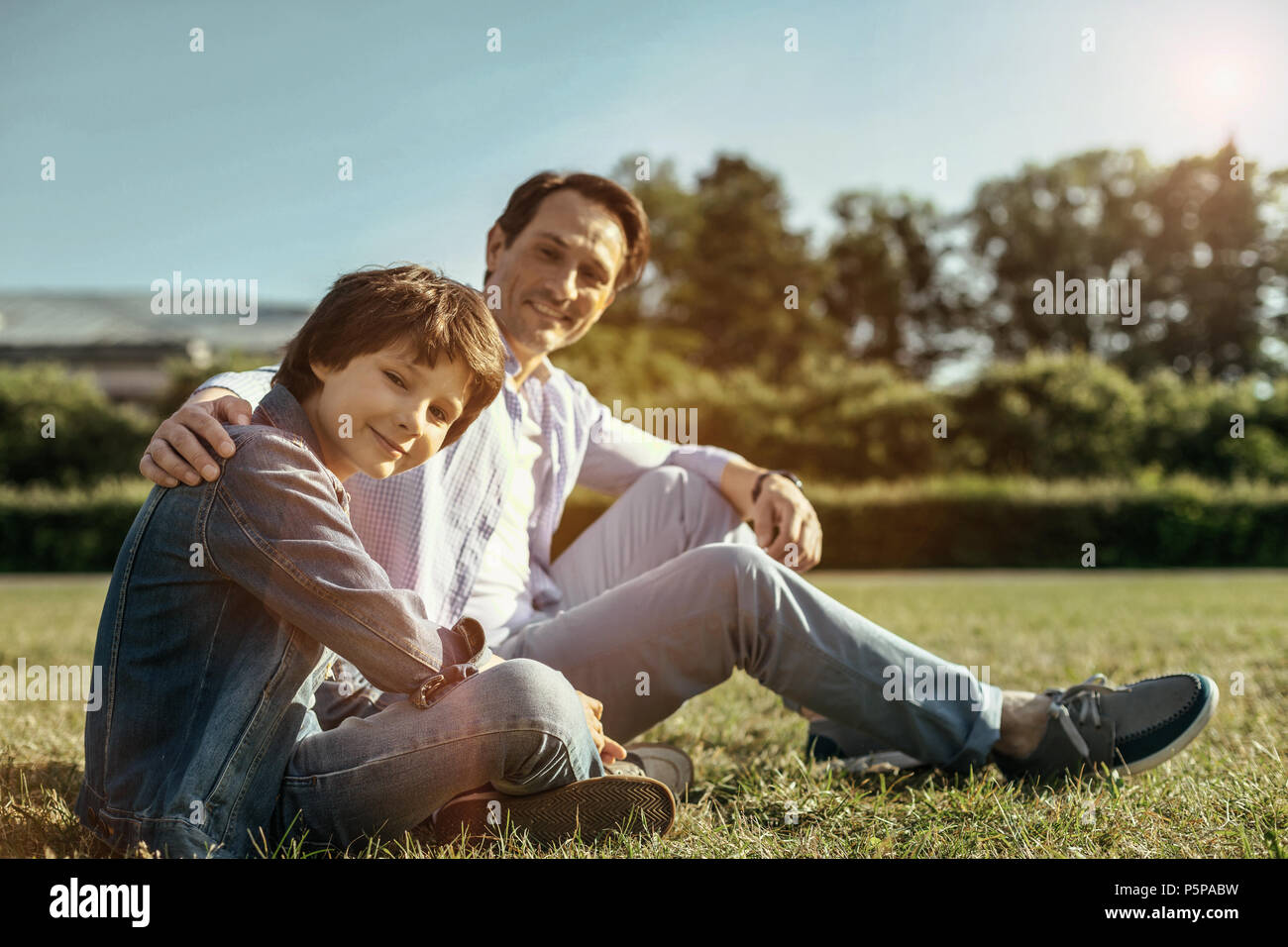 Dad and son sitting on the grass smiling and hugging Stock Photo - Alamy