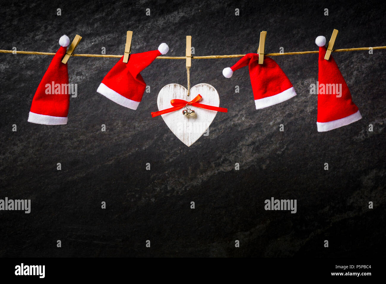 Dark christmas background with santa hats and heart on a rope Stock Photo