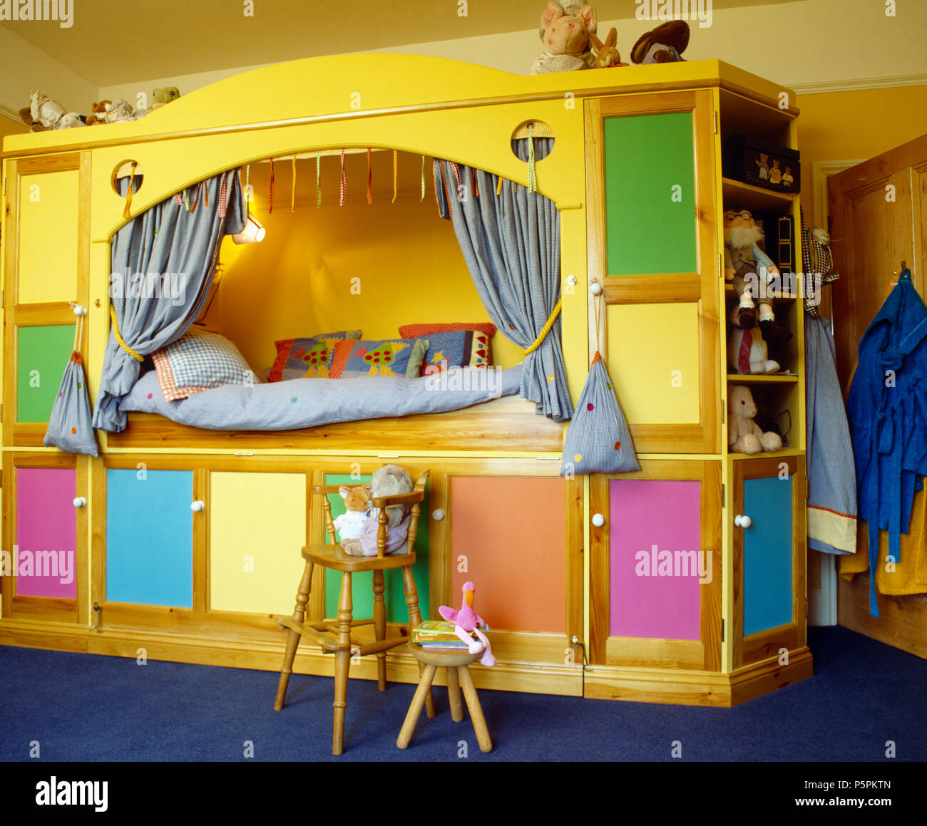Yellow built-in platform bed with colourful doors on under-bed storage in child's bedroom Stock Photo