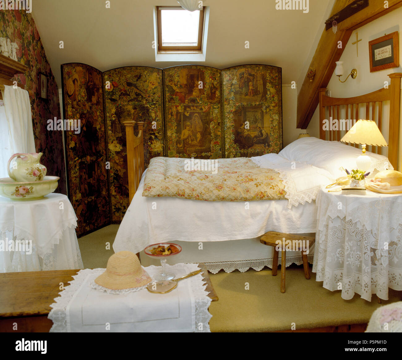White quilt and vintage eiderdown on bed in attic bedroom with Victorian decoupage screen and white, broderie-Anglaise edged cloths on tables Stock Photo