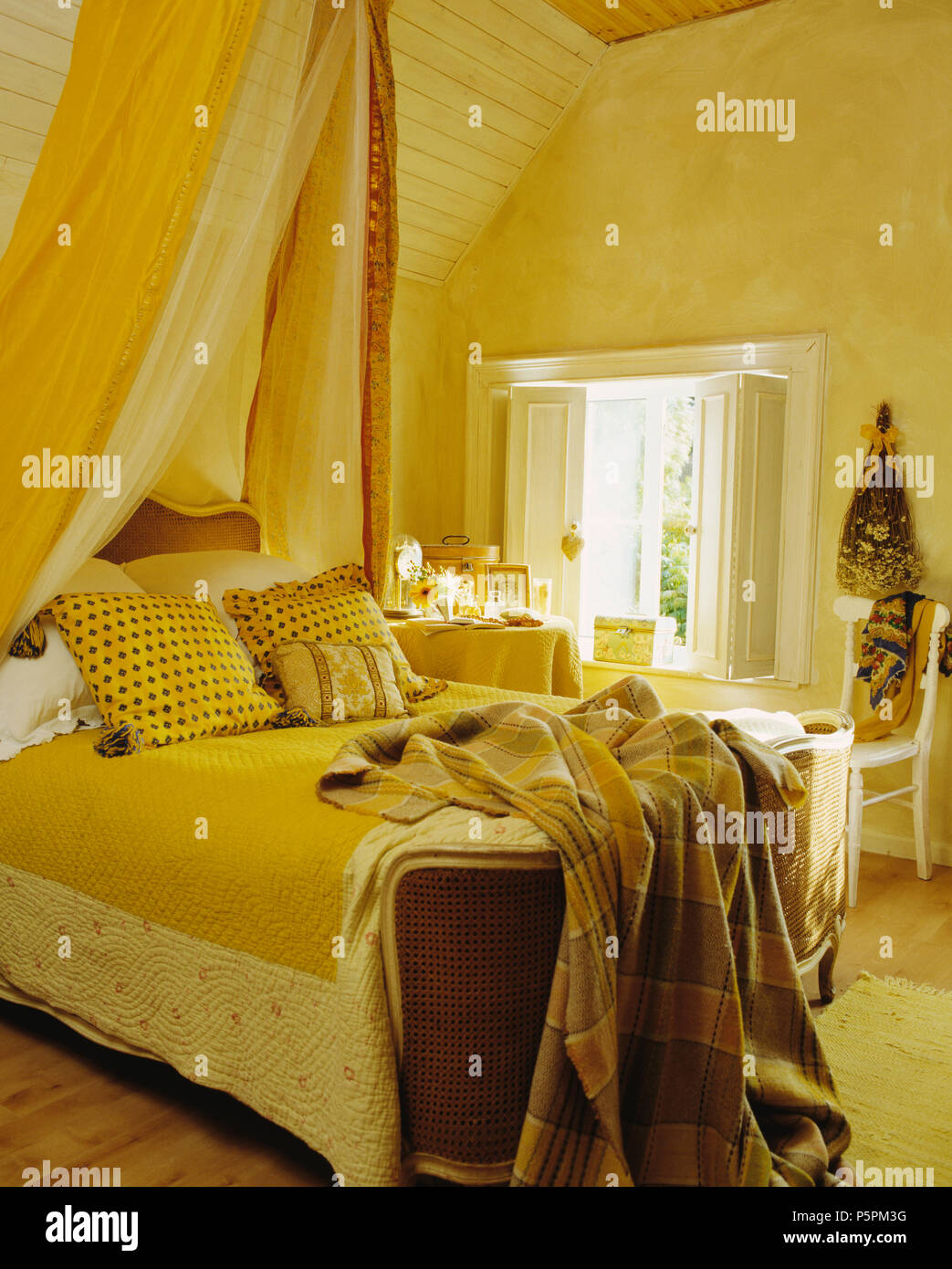 Yellow drapes above French bed with yellow quilt and checked throw in pastel yellow country bedroom Stock Photo