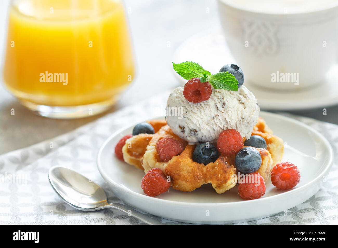Homemade waffles with ice cream and fresh berries-raspberries, blueberries.  Delicious dessert, cappuccino and orange juice on the table. Selective foc  Stock Photo - Alamy