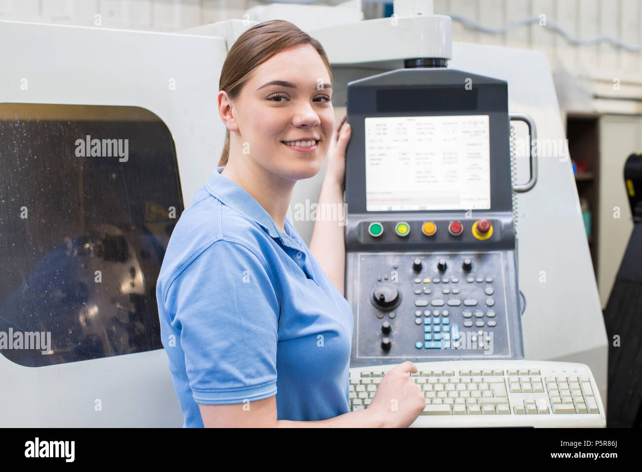 Portrait Of Female Apprentice Engineer Operating CNC Machine In Factory Stock Photo