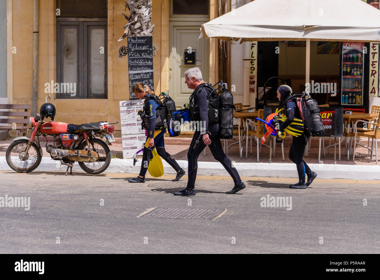 Three divers wearing full scuba gear walk down a street in Gozo, Malta Stock Photo