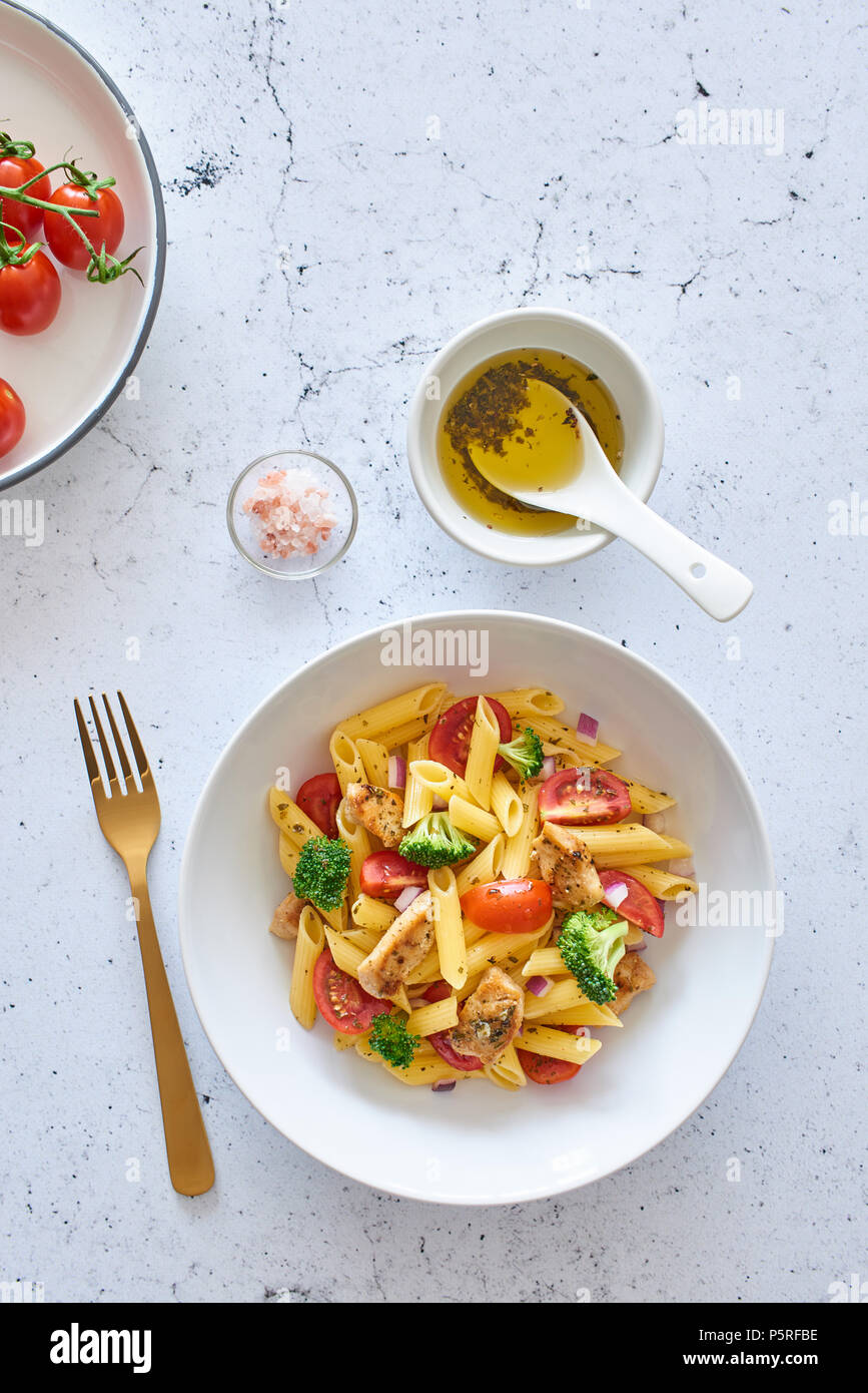 Italian food. Flat lay of fusilli pasta salad with italian dressing, tomatoes, broccoli and basil leaves on white marble background. Top view. Stock Photo