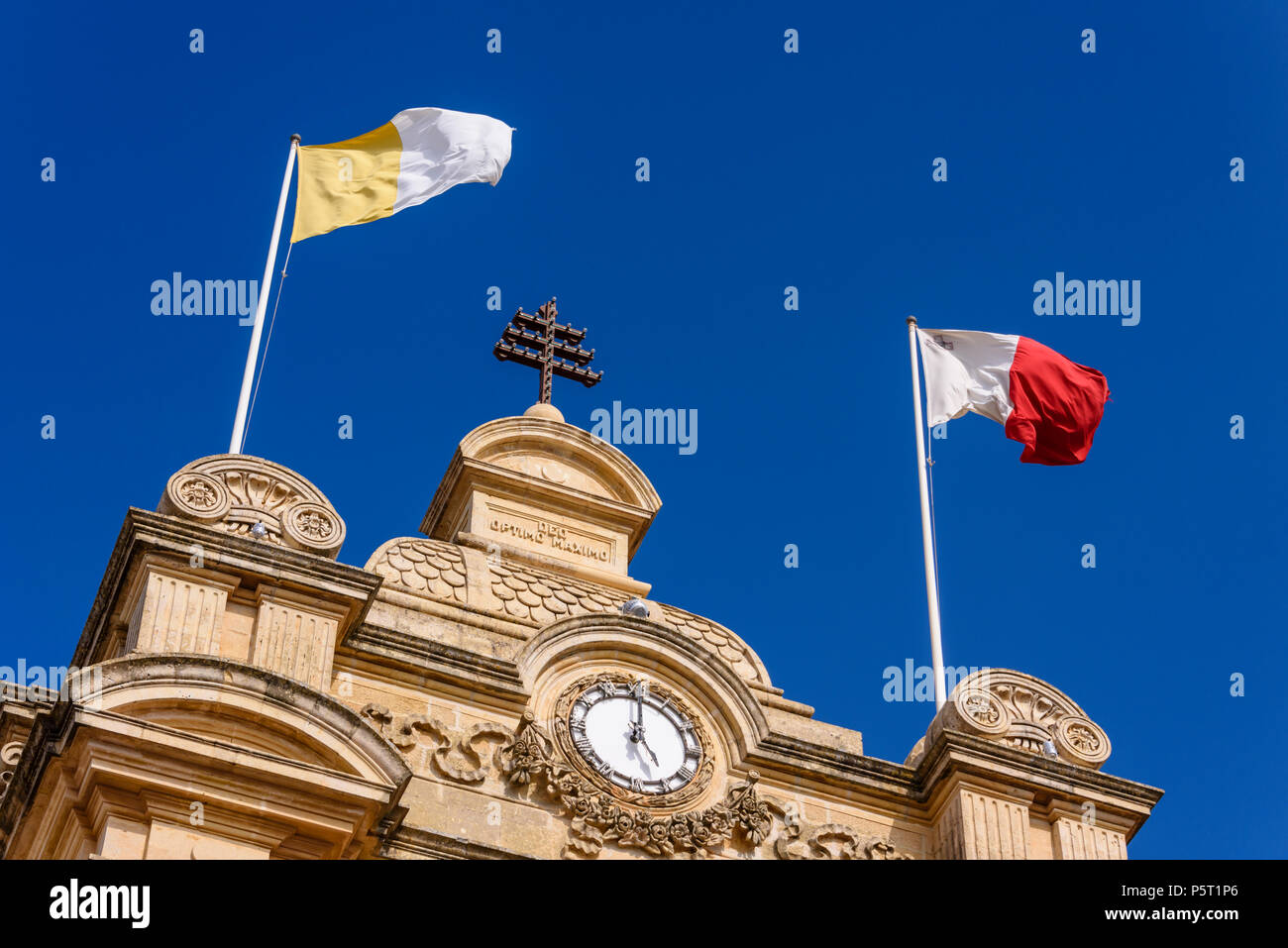 The flag of Saint Paul and the Malta flag fly from Nadur Church, which is topped buy a Papal cross. Stock Photo