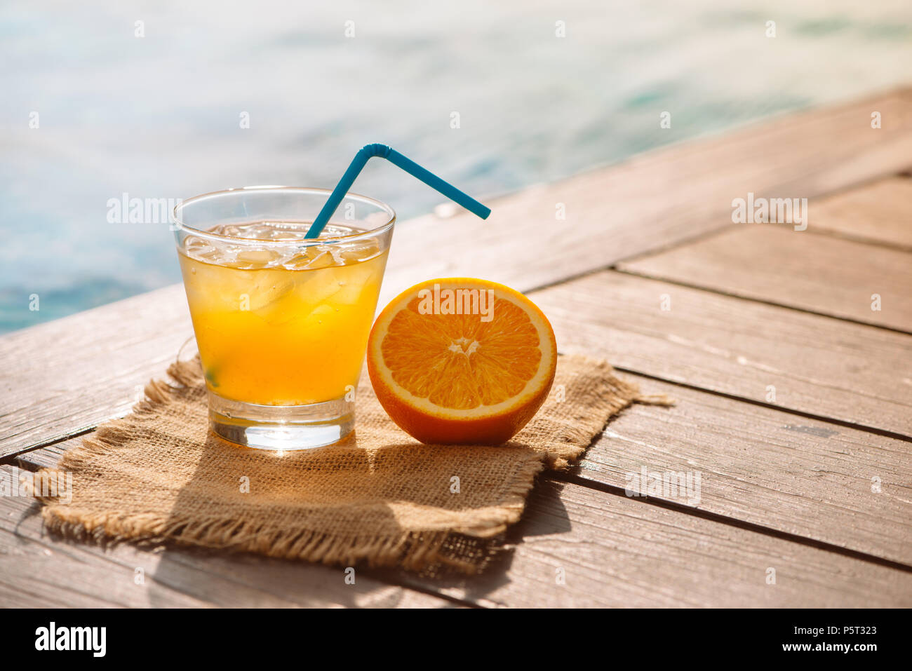 Close up of screwdriver cocktail alcohol drink with orange juice, slices and ice standing near the pool. Refreshing iced lemonade beverage in glass by Stock Photo