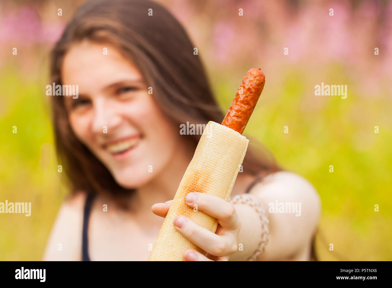 Young smiling girl offering a hot dog for us, focus on it. Summer sunny day Stock Photo